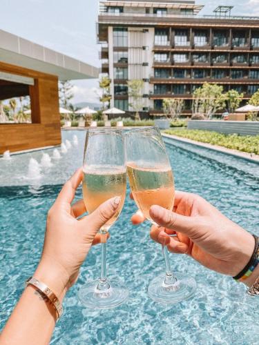 two people holding wine glasses in front of a swimming pool at 1 Hotel Haitang Bay, Sanya in Sanya