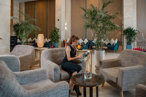 a woman sitting on a chair reading a book in a lobby at Diamond Sea Hotel in Da Nang