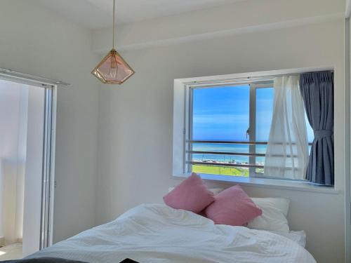 - un lit avec des oreillers roses dans une chambre avec une fenêtre dans l'établissement vent du vent.NJ最上階, à Minatogawa