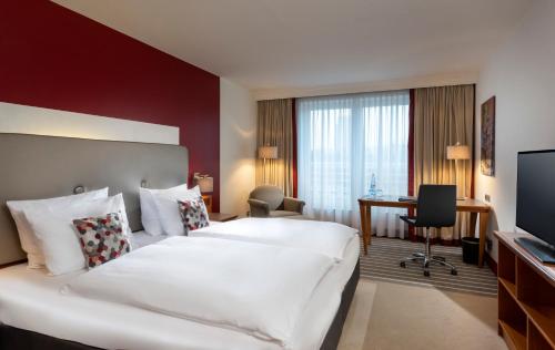 a hotel room with a large white bed and a desk at Dorint An den Westfalenhallen Dortmund in Dortmund