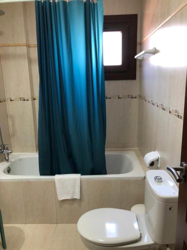 a bathroom with a toilet and a blue shower curtain at Cotillo Ocean View in Cotillo