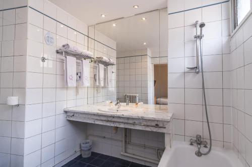a white tiled bathroom with a sink and a tub at Hotel Ours Blanc - Victor Hugo in Toulouse