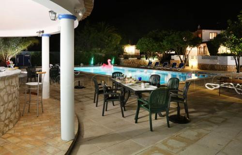 una mesa y sillas junto a una piscina por la noche en CASA BEACHCOMBER Le jardin des Arts, en Lagos