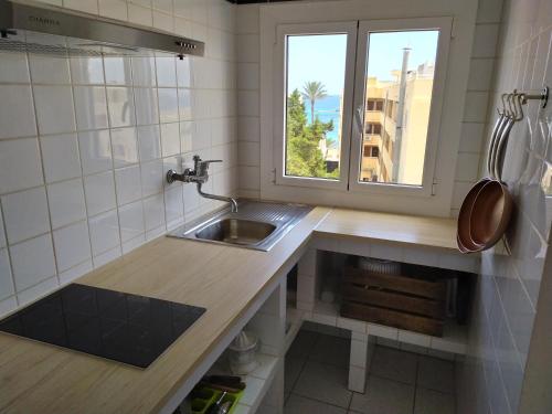eine kleine Küche mit einem Waschbecken und einem Fenster in der Unterkunft Bonito apartamento a 20m del mar in Es Pujols