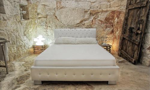 Cama blanca en habitación con pared de piedra en Puntebianche B&B, en Ceglie Messapica
