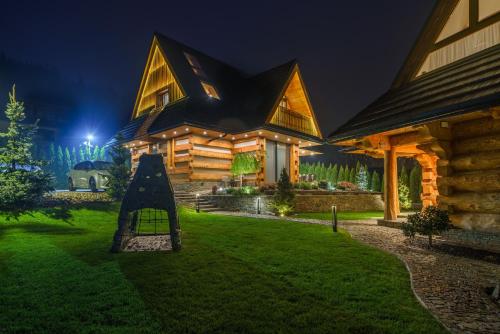 una casa di tronchi di notte con un parco giochi di fronte di Luxury Chalet Wioska Jagny a Poronin