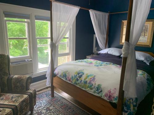 een slaapkamer met een bed, een stoel en ramen bij Green Oaks B&B in Niagara on the Lake