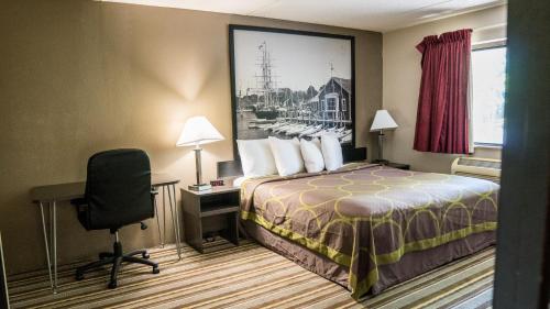 a hotel room with a bed and a desk and a chair at Super 8 by Wyndham Groton in Groton