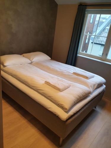 a bed with white sheets and pillows next to a window at Nygårdsgaten apartments in Bergen