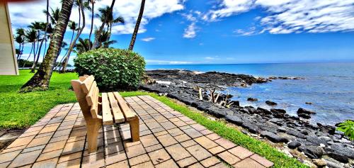 a wooden bench sitting on a brick path near the ocean at Ali'i Banyan Breeze in Kailua-Kona