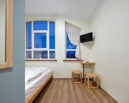 a bedroom with a bed and a table and two windows at DREAM Hostel Khmelnytskyi in Khmelʼnytsʼkyy