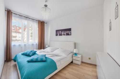 a white bedroom with a bed with blue pillows on it at Apartamenty Sun & Snow Port II in Kołobrzeg