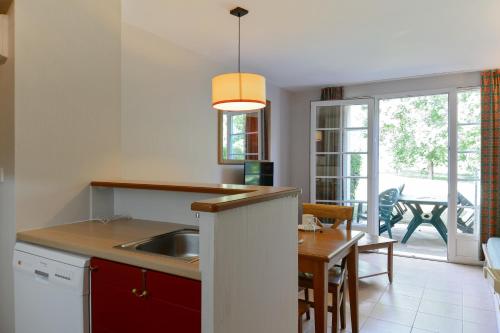 a kitchen with a sink and a dining room with a table at Residence du Lac - maeva Home in Monflanquin