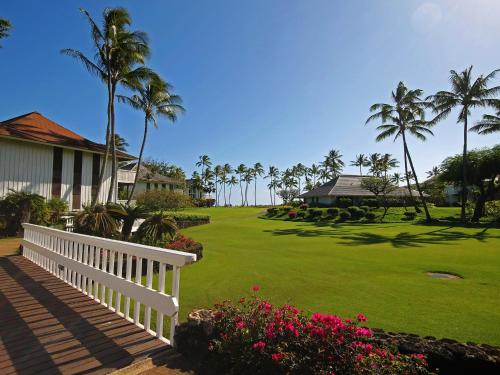 a house with a white fence and a yard with palm trees at Castle Kiahuna Plantation & Beach Bungalows in Koloa