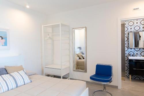 a white bedroom with a blue chair and a mirror at Guest House Bella Onda in Tessera