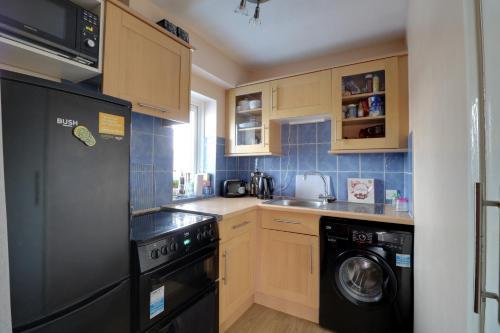 La cuisine est équipée d'un réfrigérateur noir et d'un lave-vaisselle. dans l'établissement Luxury Studio Apartment, à Northolt