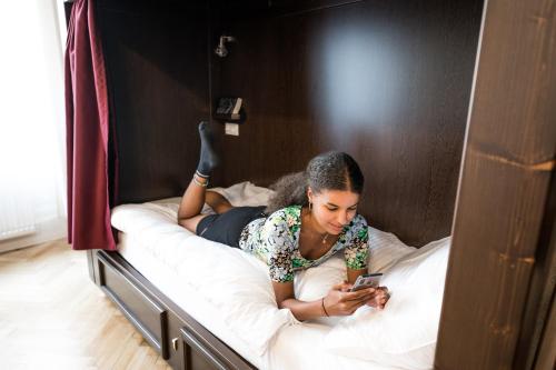 a woman laying on a bed looking at her cell phone at Vienna Boutique - Premium Hostel in Vienna