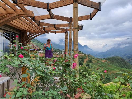 a woman standing under a wooden pergola with roses at Sapa Clay House - Mountain Retreat in Sa Pa