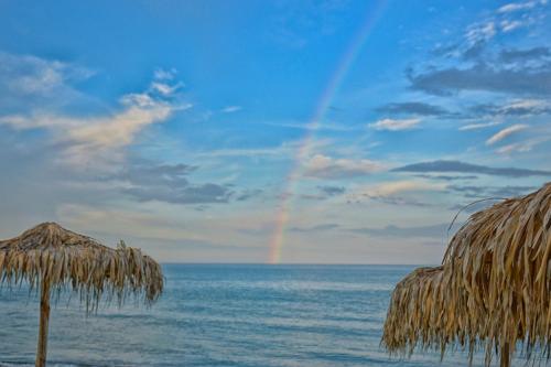 a rainbow in the sky over a beach with a straw umbrella at Майстор Костадин - 1878 in Obzor