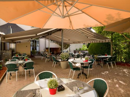 un patio al aire libre con mesas, sillas y sombrillas en Hôtel - Restaurant " Victor Hugo", en Vianden