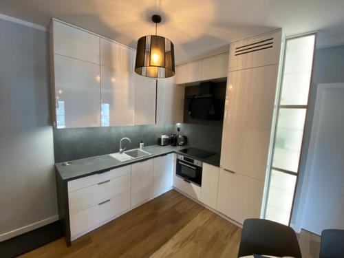 a kitchen with white cabinets and a sink and a light at Apartament SZAFIROWY Gardenia Dziwnów z widokiem na morze in Dziwnów