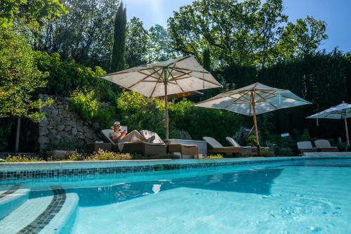une femme assise sur une chaise à côté d'une piscine avec parasols dans l'établissement domaine des tilleuls d'or, à Saint-Cézaire-sur-Siagne