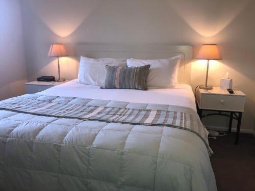 a bedroom with a large white bed with two lamps at Tuscana Motor Lodge in Christchurch