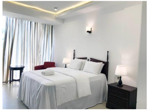a white bedroom with a large bed and a red chair at Bayfront in Weligama