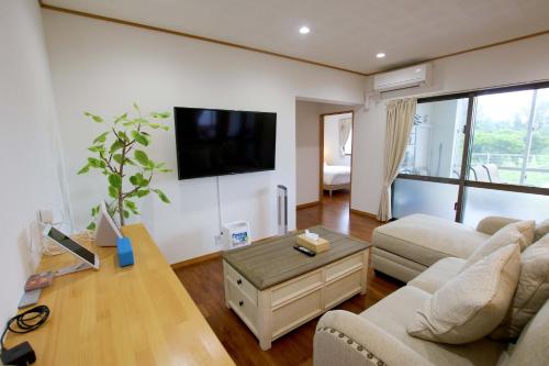 a living room with a couch and a tv on the wall at Beach Side Secret in Ginoza