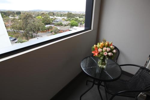 a glass table with a vase of flowers on it next to a window at Melbourne Knox Central Apartment Hotel Official in Wantirna