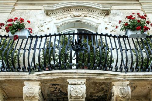 a balcony with red flowers on a building at Bed and Breakfast Terra del Sole Ibla in Ragusa