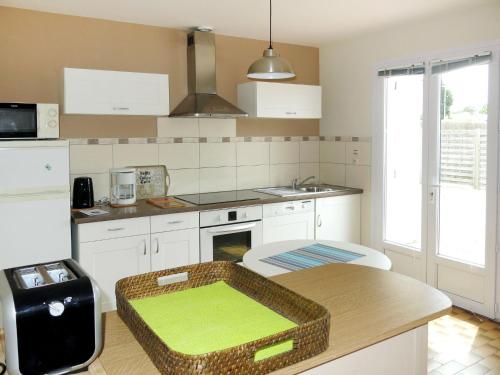 une cuisine avec des placards blancs et une table avec un coussin vert dans l'établissement Holiday Home Le Maupas by Interhome, à La Tranche-sur-Mer