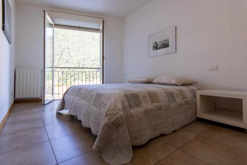a white bedroom with a bed and a large window at Cozy Apartment Mati Lago Maggiore in Verbania