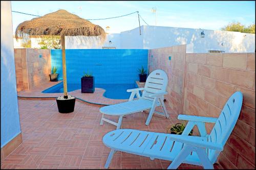 two blue chairs and an umbrella on a patio at Chalet 2 dormitorios con piscina privada in Conil de la Frontera