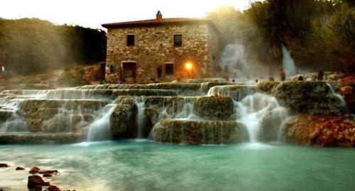 una cascata di fronte a un edificio in pietra con un edificio di La Casa del Villanu a Pitigliano