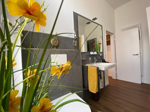 ein Badezimmer mit einem Waschbecken, einem Spiegel und gelben Blumen in der Unterkunft Quartier 1903 in Oldenburg
