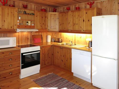 uma cozinha com armários de madeira e um frigorífico branco em Chalet Saglia - SOO020 by Interhome em Mjåvatn