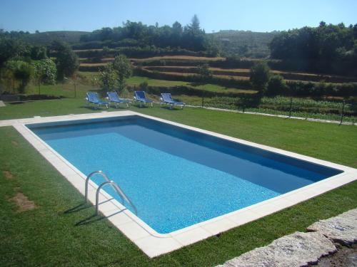 a swimming pool in a yard with two chairs and a field at Casa dos Bernardos in Terras de Bouro