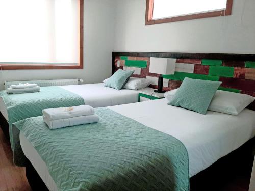 a room with three beds with green and white sheets at Hostal Buenavista Patagonia in Punta Arenas