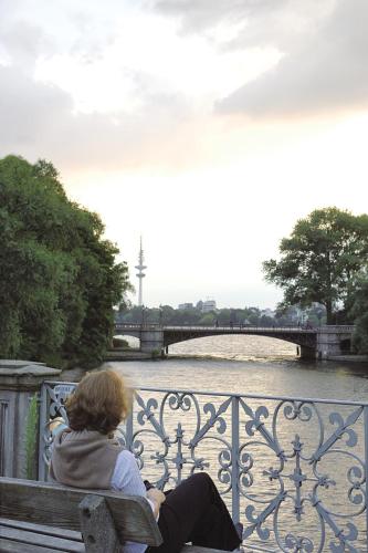a woman sitting on a bench next to a river at Hotel Miramar in Hamburg