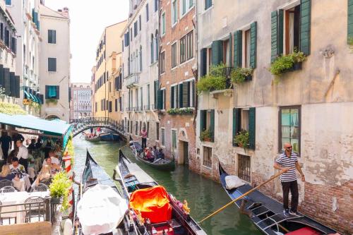 Um homem está a remar duas gôndolas por um canal. em Residence Suite a Venezia em Veneza