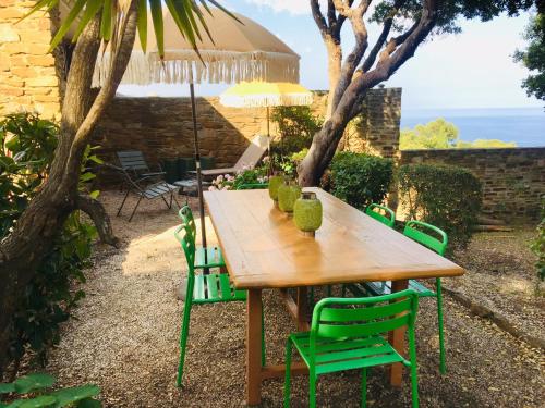 a wooden table with green chairs and an umbrella at Gaou Benat, village des fourches, Label patrimoine XXe siècle in Bormes-les-Mimosas