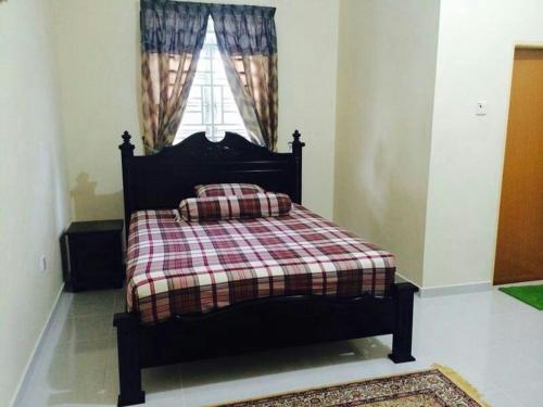 a bedroom with a bed with a plaid blanket and a window at SRI IMAN HOMESTAY KUALA TERENGGANU in Kuala Terengganu