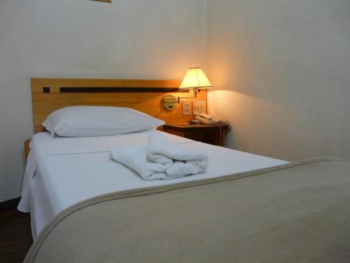 a bed with white sheets and a lamp on a table at Hotel Varginha I in Varginha