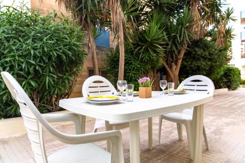a white table and chairs with wine glasses on it at Dolmen Court Flat 10, Qawra in St. Paul's Bay