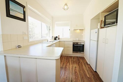a kitchen with white cabinets and a white refrigerator at Beachcomber - Pet Friendly in Merimbula