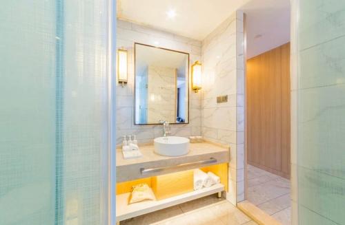 een badkamer met een wastafel, een spiegel en een douche bij Metropolo Jinjiang Wuhan Optics Valley Science and Technology Exhibition Center in Wuhan