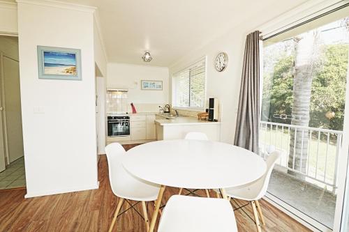 a white kitchen with a white table and chairs at Beachcomber - Pet Friendly in Merimbula