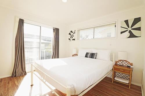 a white bedroom with a large bed and a window at Beachcomber - Pet Friendly in Merimbula
