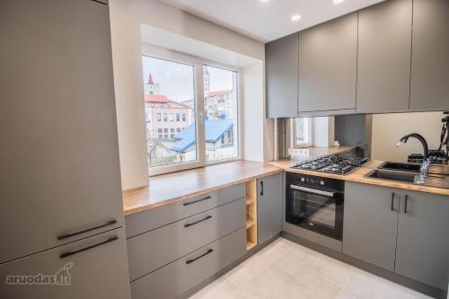 eine Küche mit weißen Schränken, einem Waschbecken und einem Fenster in der Unterkunft Jaukūs apartamentai-studija, centre in Šiauliai